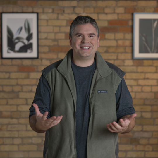 About index exchange - CEO, Andrew Casale standing smiling wearing a vest in front of a brick wall