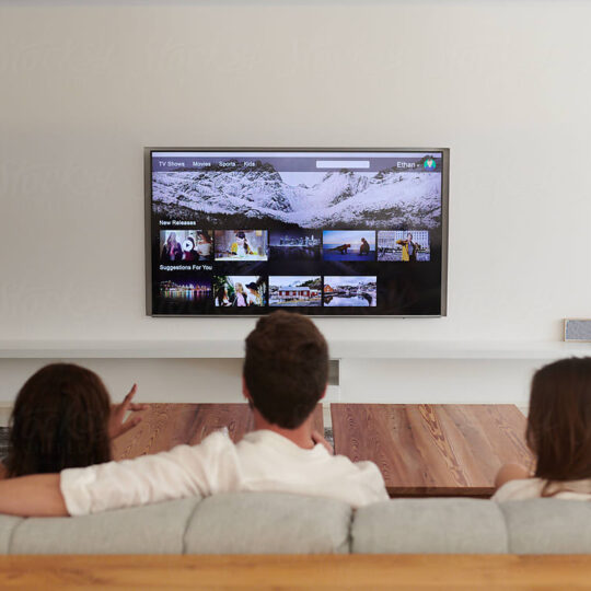 two women and a man sitting on a couch watching tv