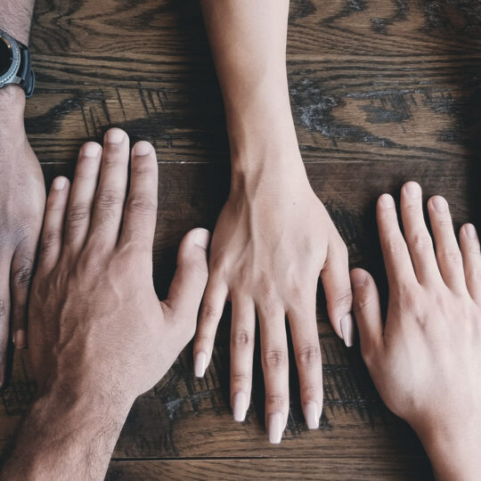 4 hands laying facedown on a wooden table