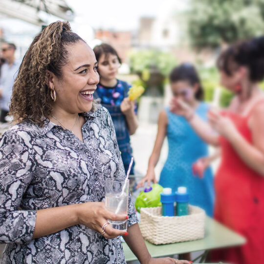 Photo d'une femme souriante buvant un cocktail sur une terrasse avec des personnes arrière plan