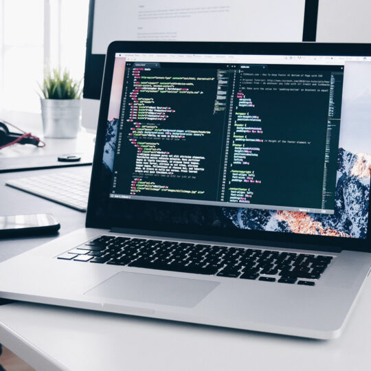 Laptop open sitting on a desk with code written across the screen