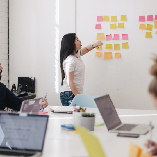 women standing up gesturing to sticky notes while a group of people look on