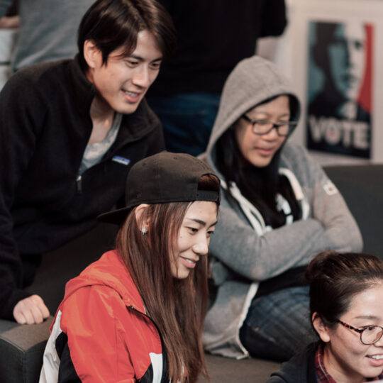 Four people sitting on a couch looking at a laptop and smiling