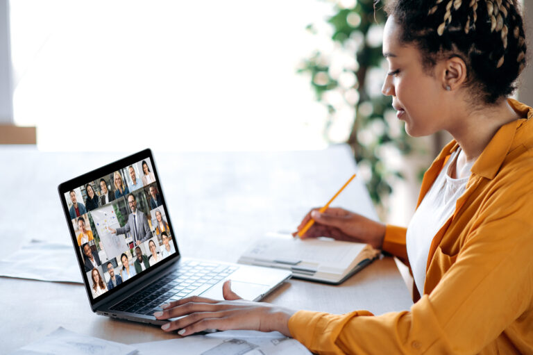 Femme assise derrière un bureau en train de visionner un webinar sur son écran d'ordinateur