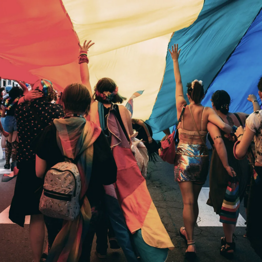 People under a rainbow flag to show Pride at Index