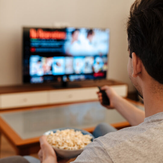 Ein Mann, von hinten fotografiert, der auf einem Sofa sitzt und sich eine Streaming-Sendung auf einem CTV ansieht