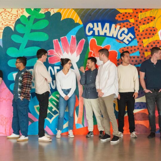 Index Exchange employees standing together, conversing in front of the office mural.