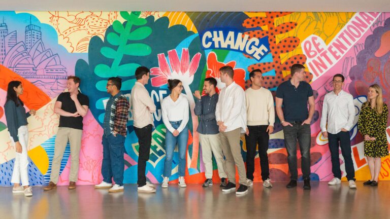 Index Exchange employees standing together, conversing in front of the office mural.