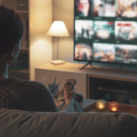 Mujer sentada en el sofá, sosteniendo un control remoto y eligiendo contenido en su smart TV.