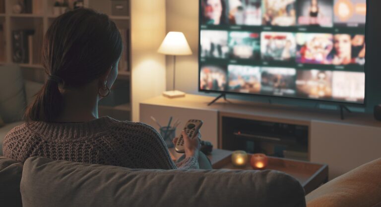 Mujer sentada en el sofá, sosteniendo un control remoto y eligiendo contenido en su smart TV.