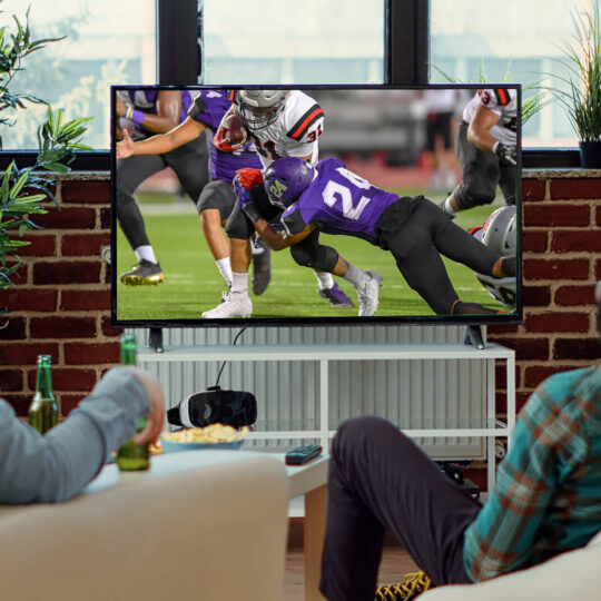 3 people siting on chairs watching college football on tv