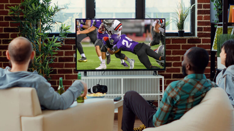 3 people siting on chairs watching college football on tv